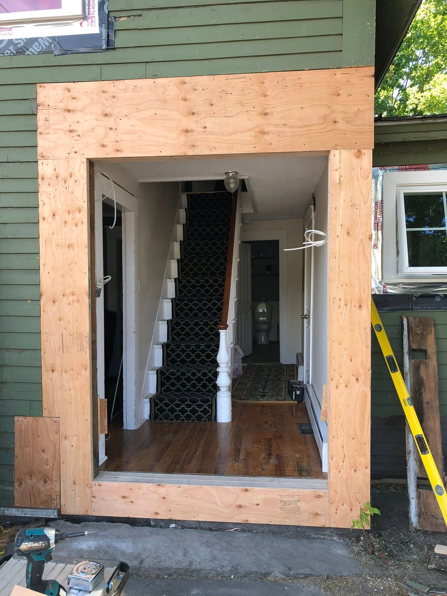 An exterior doorway frame under construction with unfinished plywood surrounding a home entrance showing stairs inside.