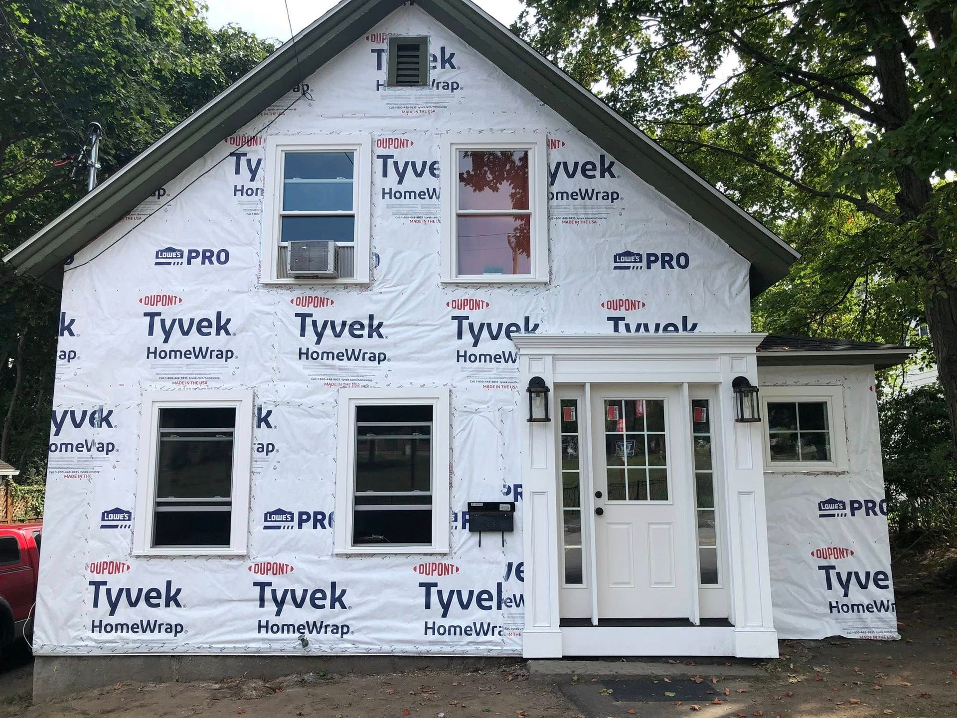 A house under construction, wrapped in white Tyvek, with a new white entryway and windows installed.