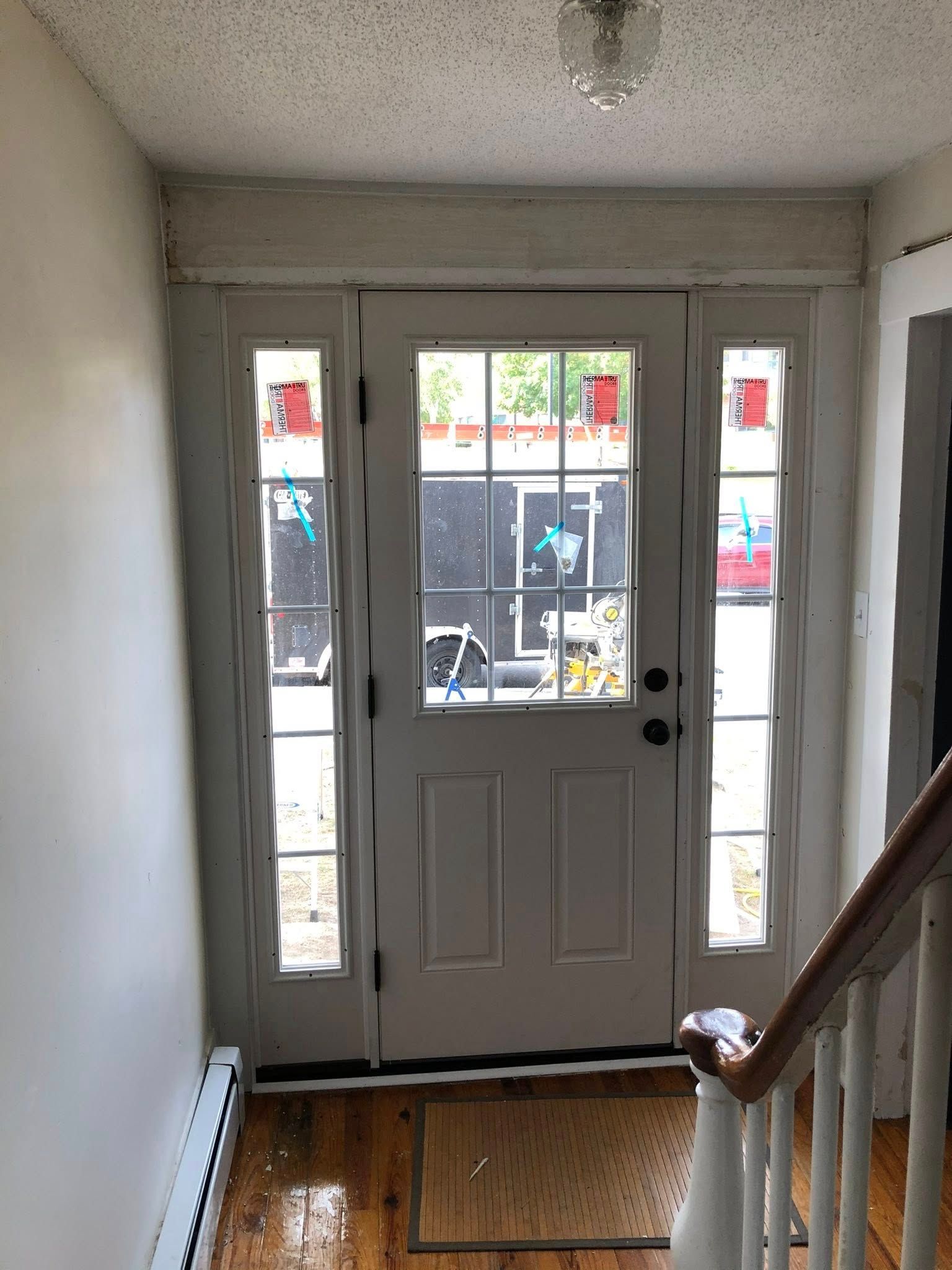 Interior view of a white front door with glass panes and side panels, leading to an outdoor walkway and stairs.