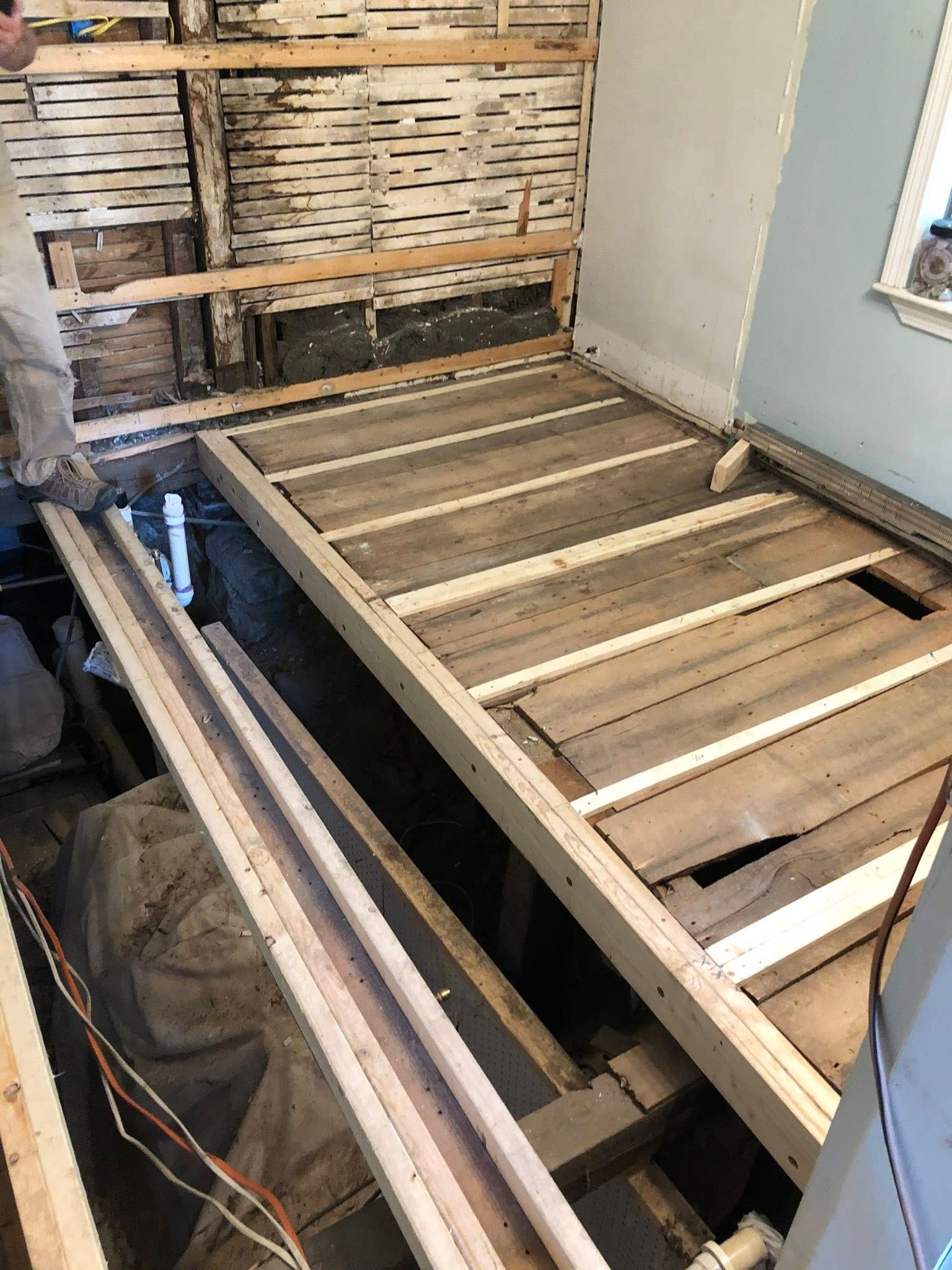 A renovation scene showing a partially exposed floor frame with wooden joists, subflooring, and open wall lath.