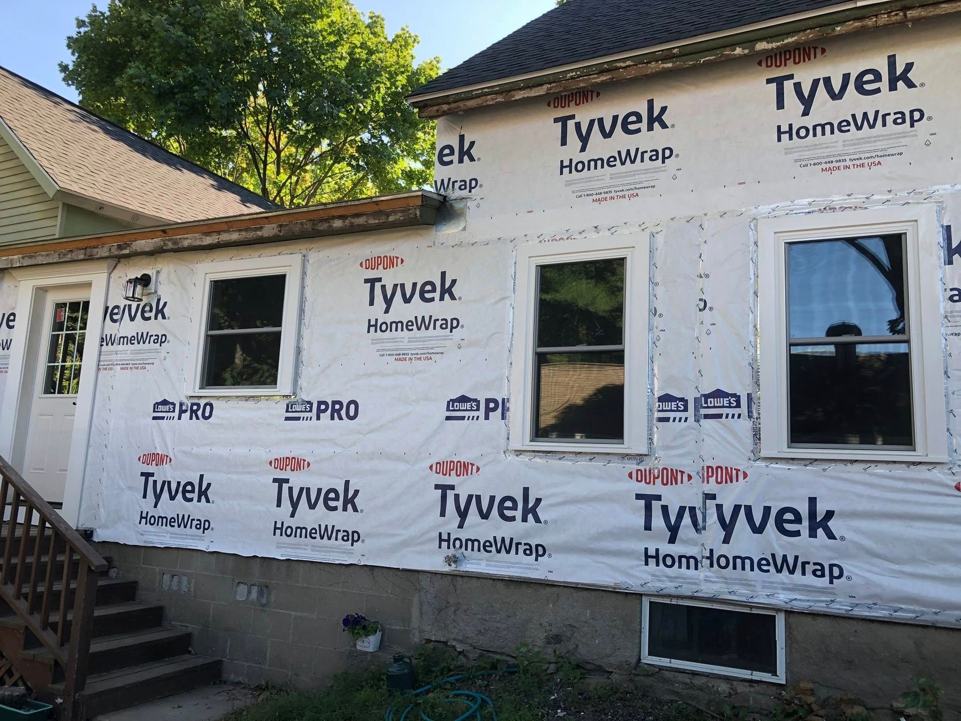 An exterior wall of a house undergoing renovations, covered in white Tyvek weather-resistant barrier wrapping.