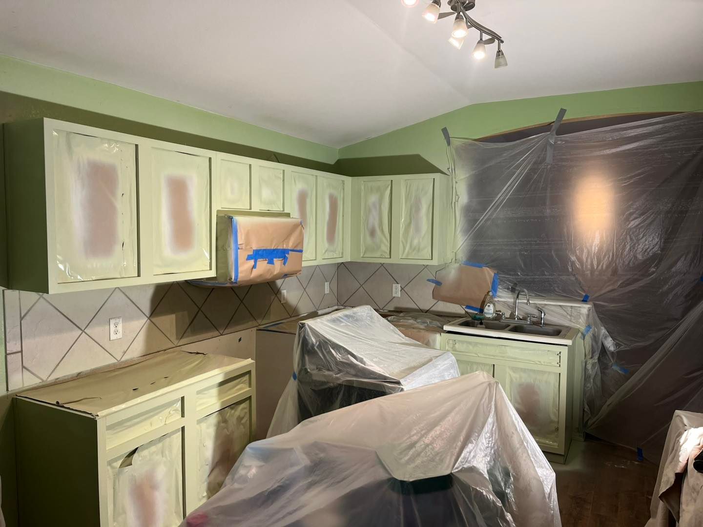 Kitchen cabinets and counters covered in plastic sheeting and painter's tape during a renovation project.