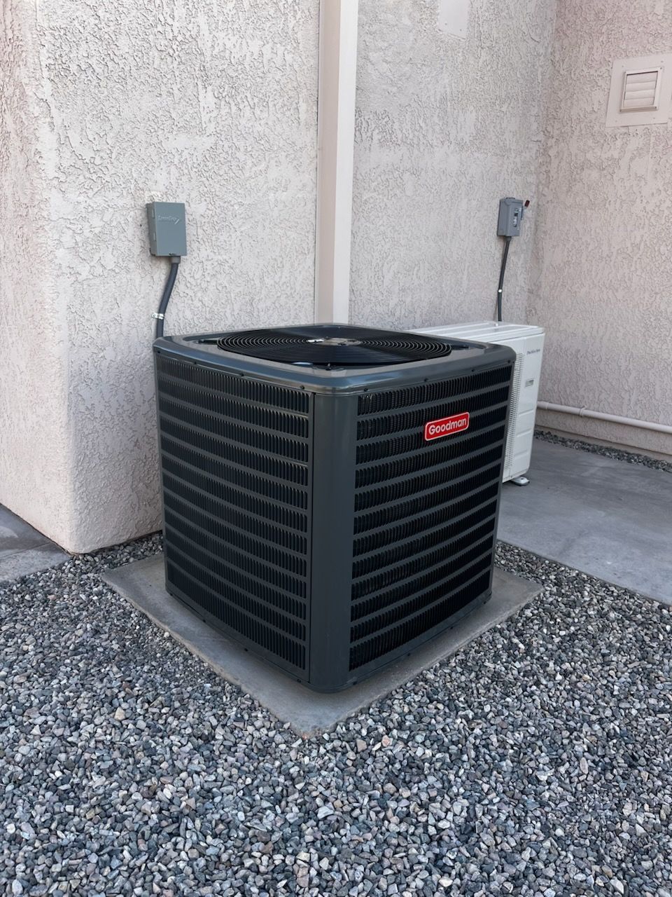 A black air conditioner is sitting on a gravel area next to a wall