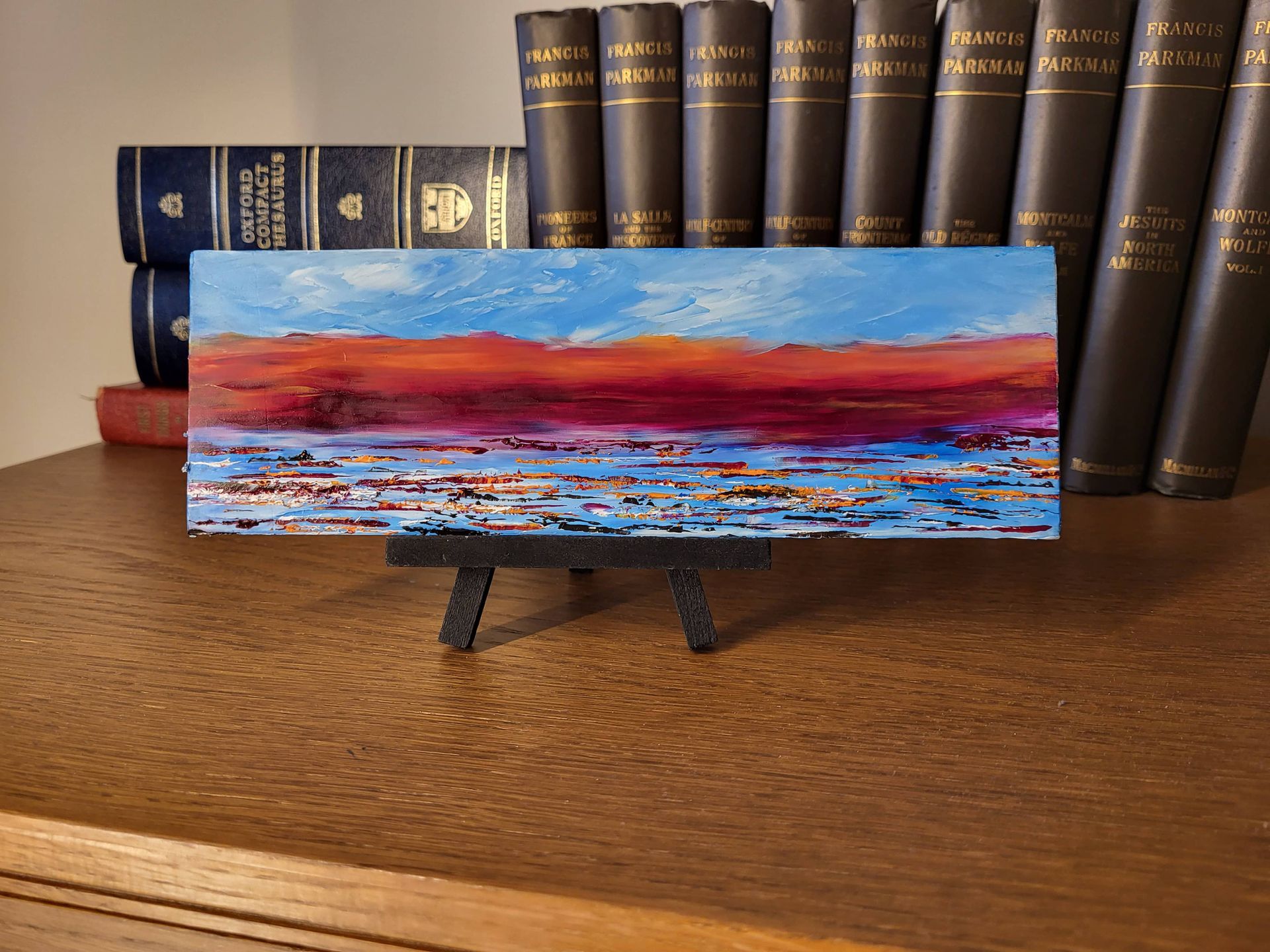 #O-72 Oil on Masonite 9 in. x 3 in. with or without  small easel. Dusk is approaching and the band of deep red and orange is in contrast to the clear blue sky. The whole scene is unfolding over a calm ocean with wavelets reflecting the reds and oranges.