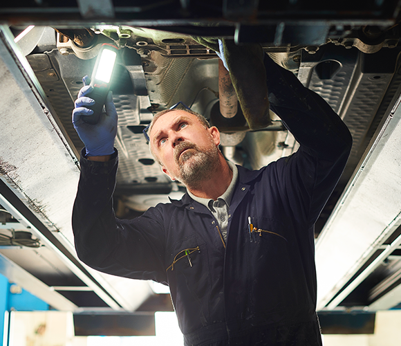 A man is working under a car with a flashlight.