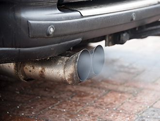 A close up of a car exhaust pipe with smoke coming out of it.