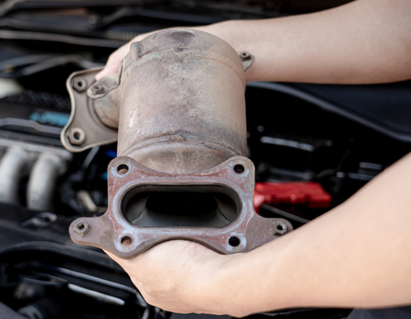 A person is holding a exhaust pipe in their hands in front of a car engine.