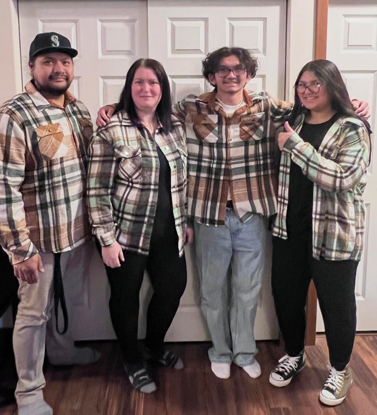 Family of four wearing plaid shirts and black pants, posing in front of a white door.