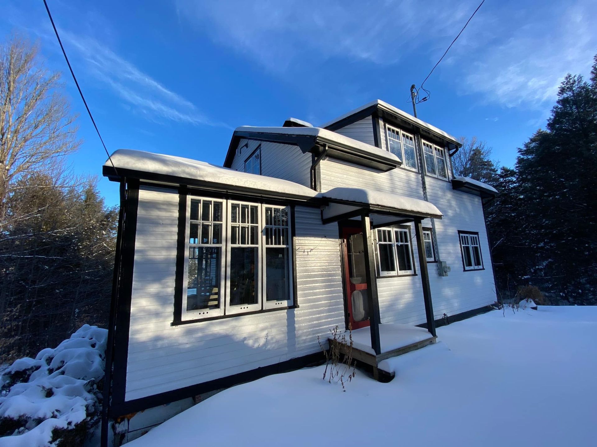 A white house with black trim is covered in snow.