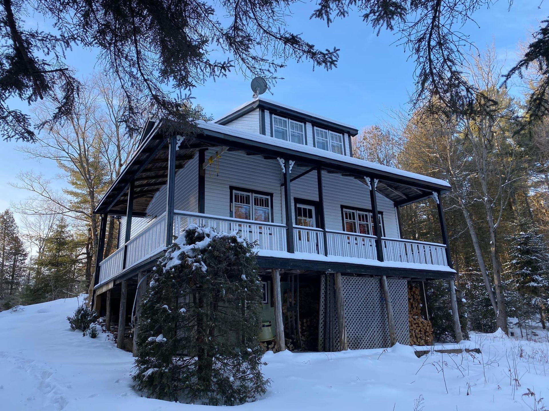 A large white house with a large porch is surrounded by snow and trees.