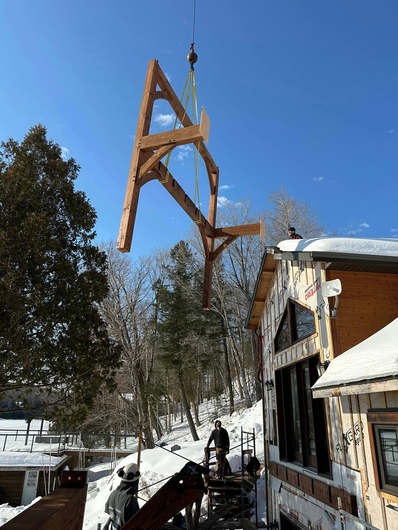 Une grande structure en bois est soulevée dans les airs par une grue.
