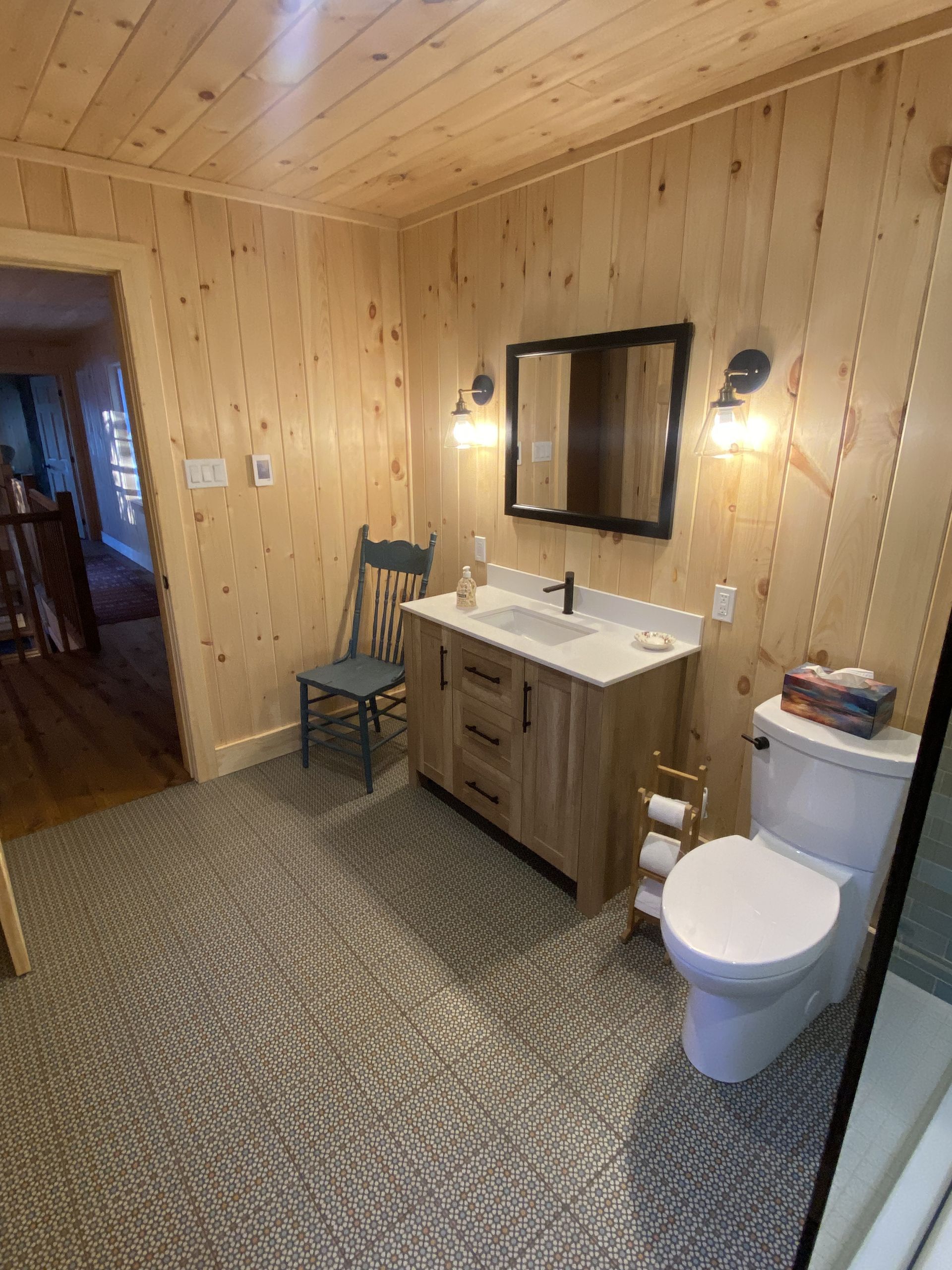 A bathroom with a sink , toilet , mirror and chair.