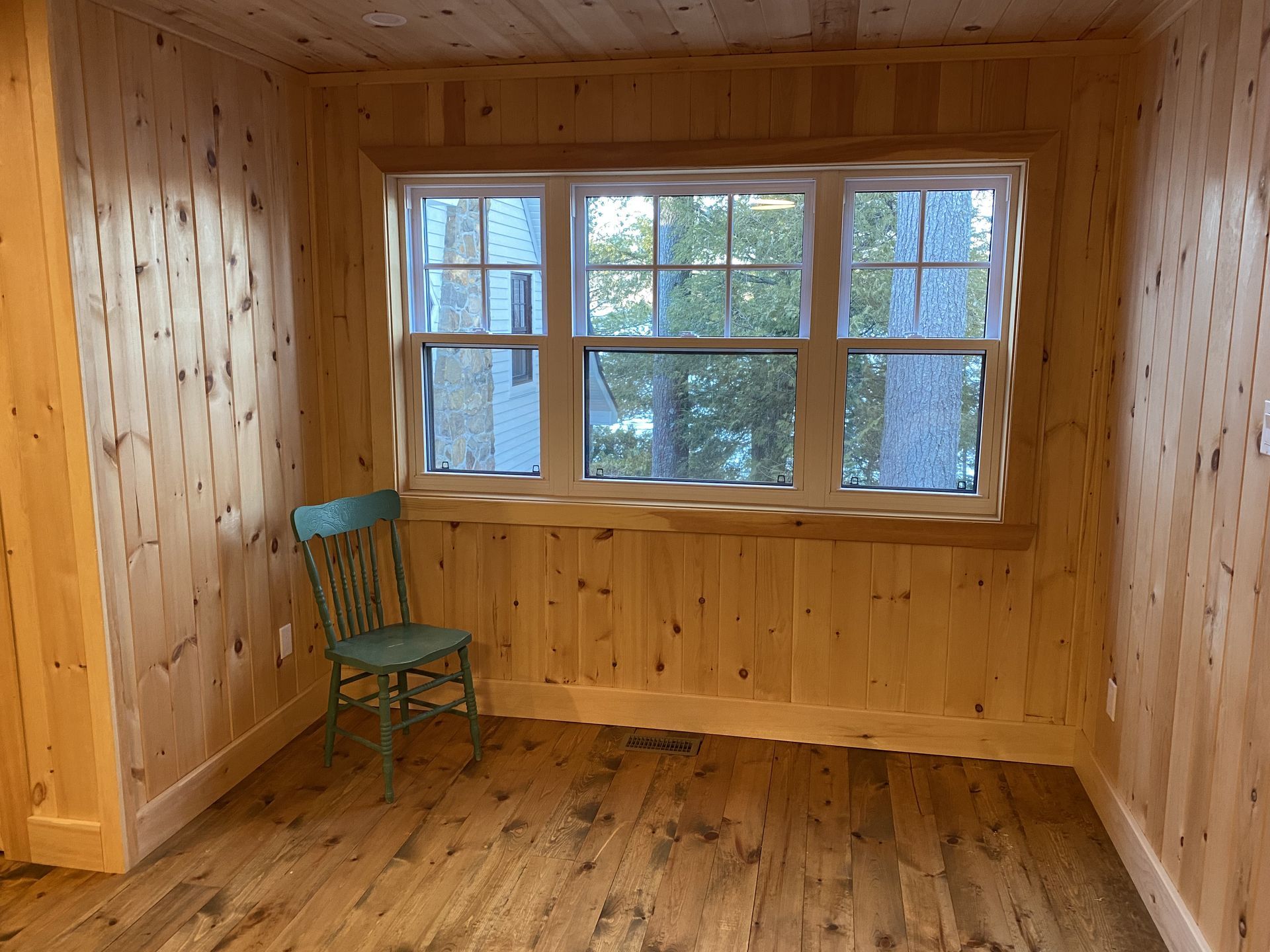 A room with wood paneling and a chair in front of a window.