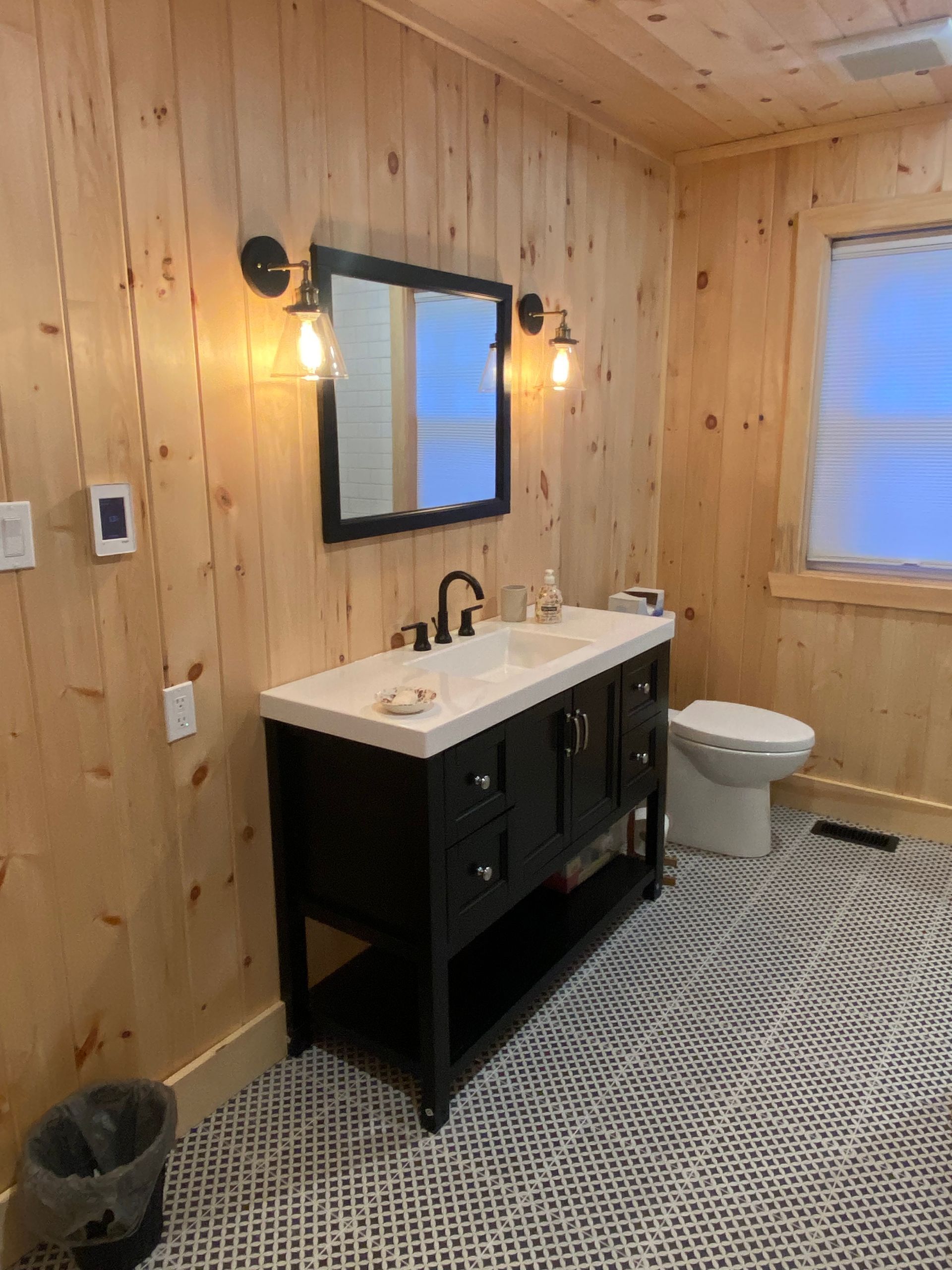 A bathroom with a sink , toilet , mirror and wooden walls.