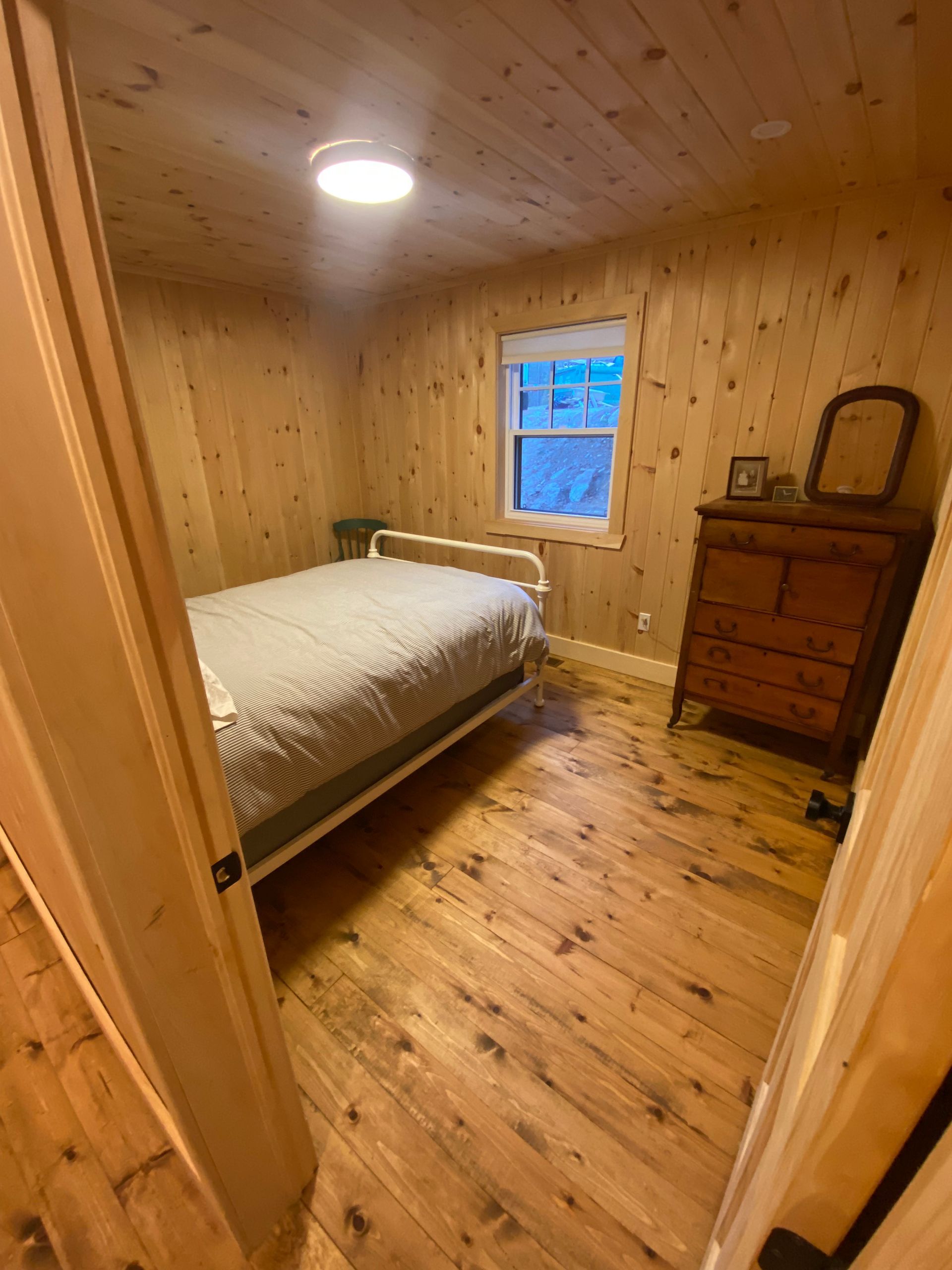 A bedroom with a bed , dresser , mirror and window.