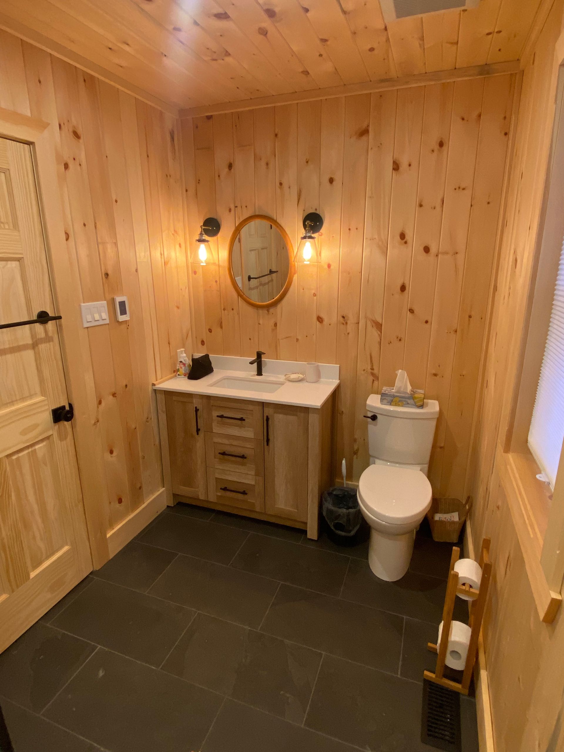 A bathroom with a sink , toilet , mirror and wooden walls.