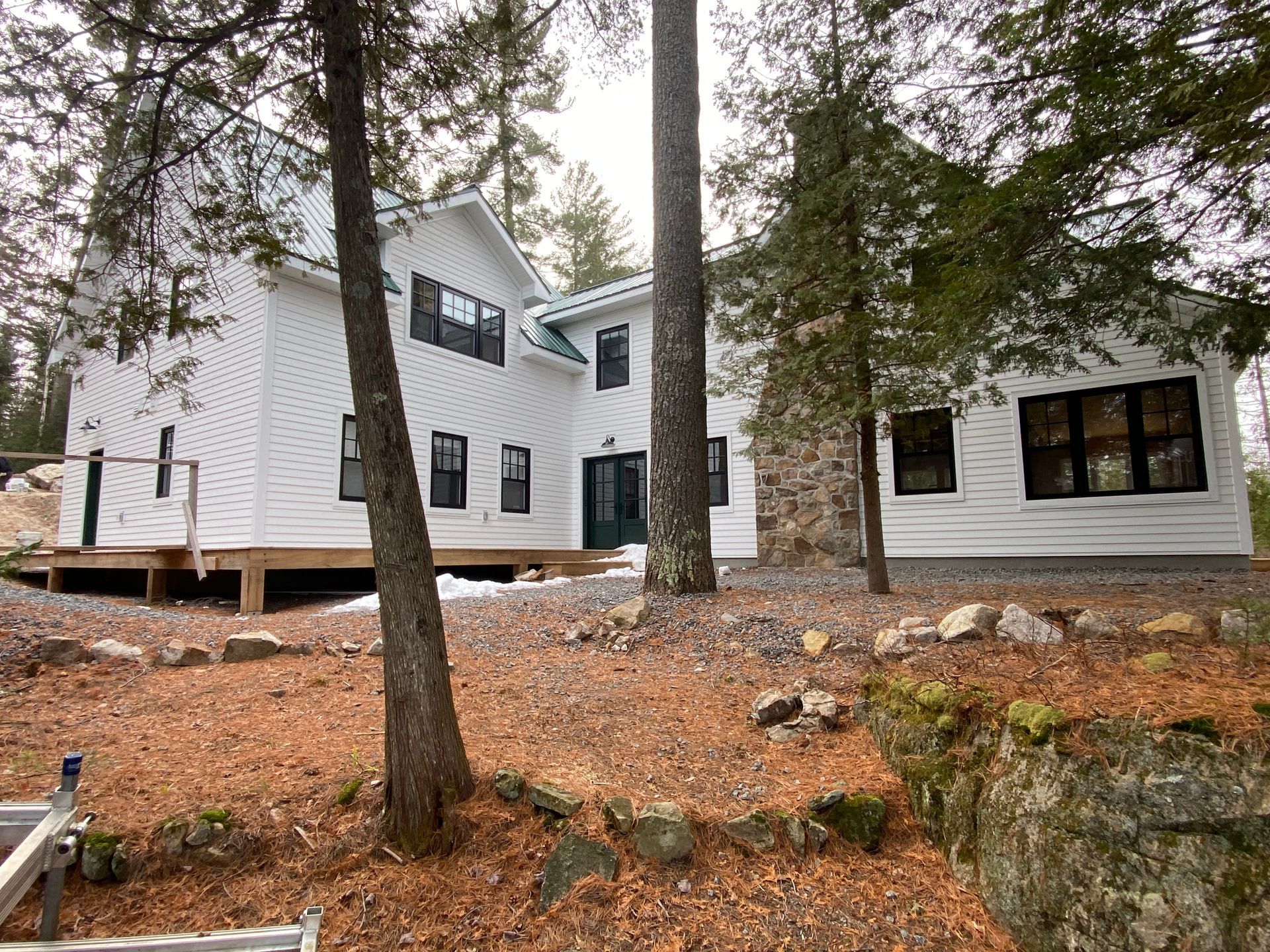 A large white house is surrounded by trees and rocks.