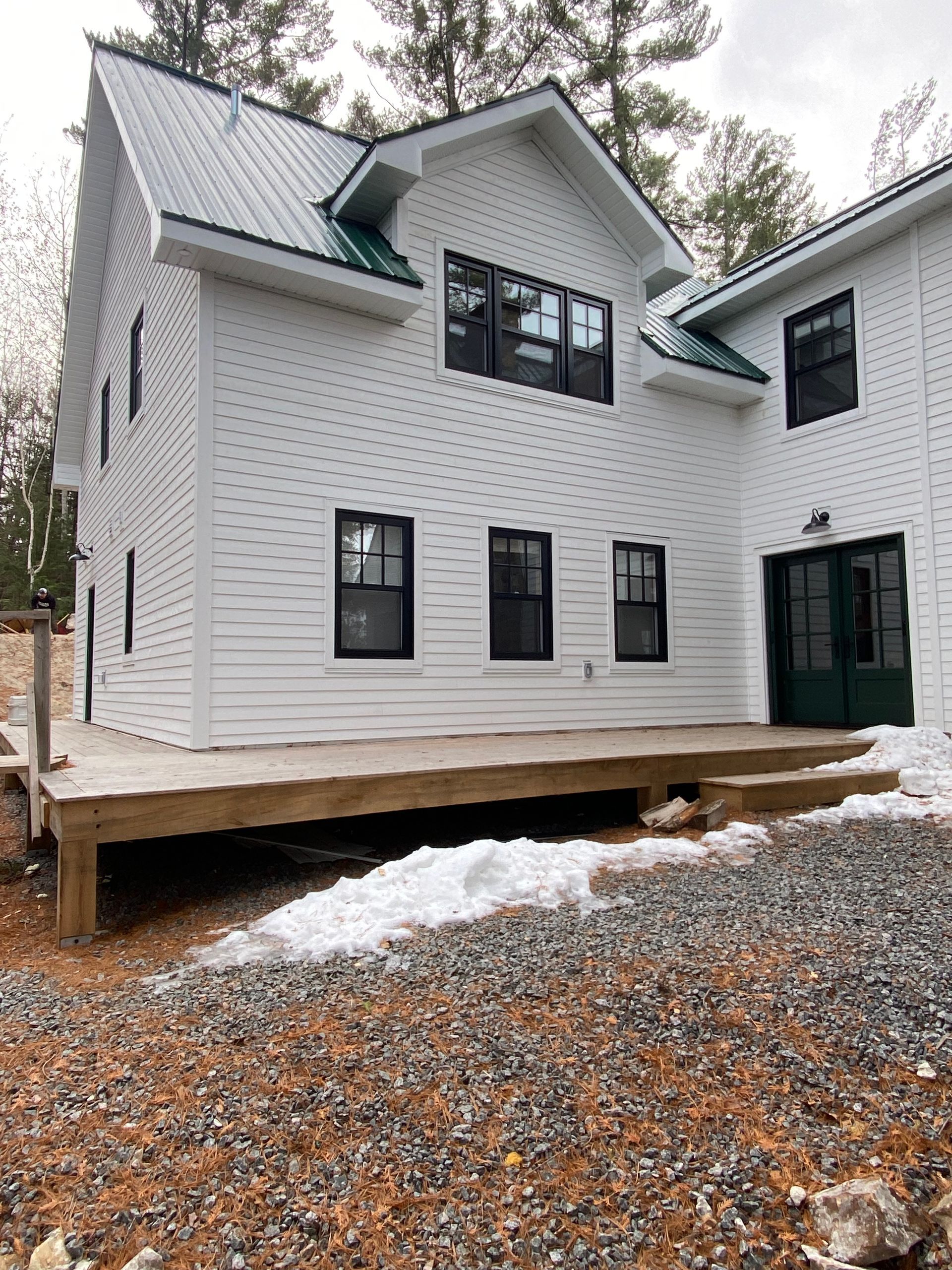 A white house with a green roof and a wooden deck.