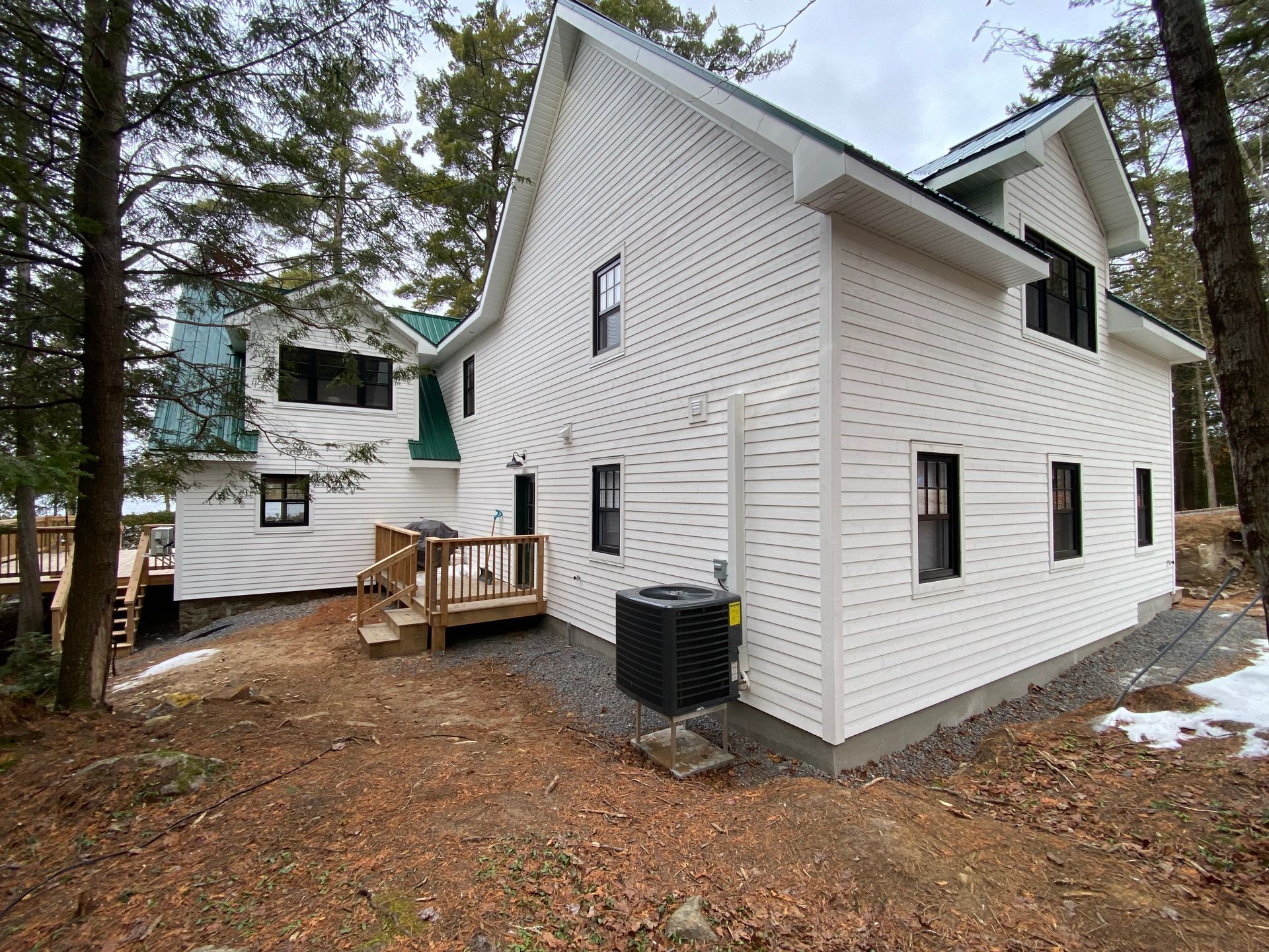 A white house with a green roof is surrounded by trees.