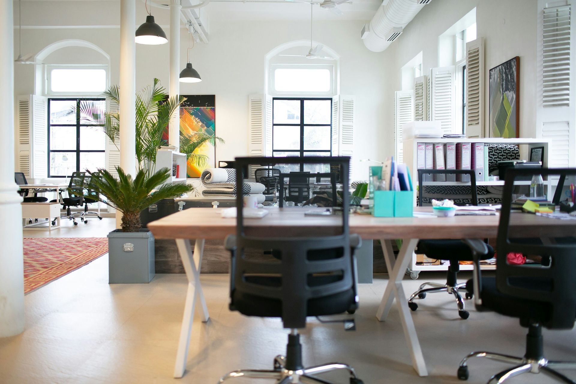 A bright office space showing  several desks and office chairs.