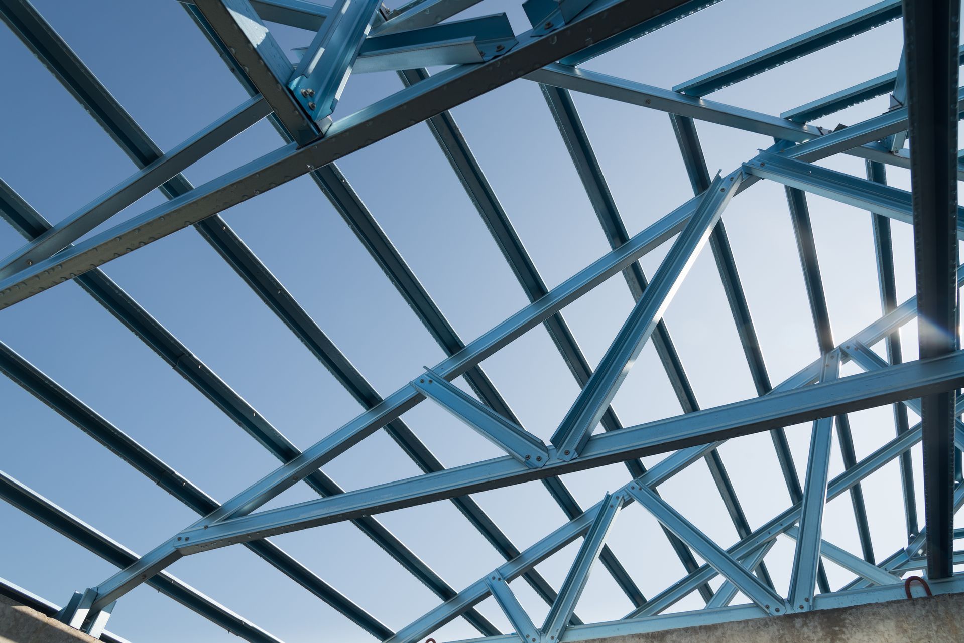 Blue metal roof trusses against a bright blue sky.