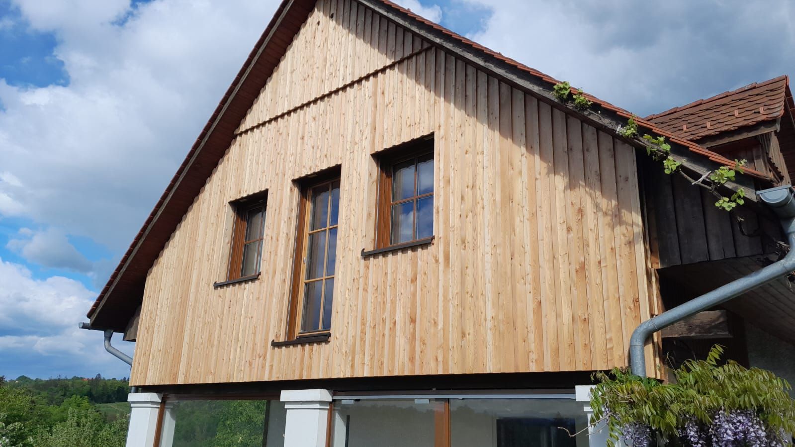 Ein Haus mit einer Holzfassade, einem Dach und vielen Fenstern.