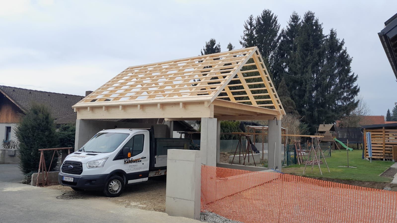 Ein weißer Lieferwagen steht vor einem Holzcarport im Bau.