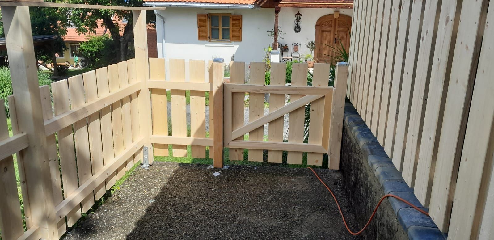 Ein Holzzaun mit einem Tor vor einem Haus.