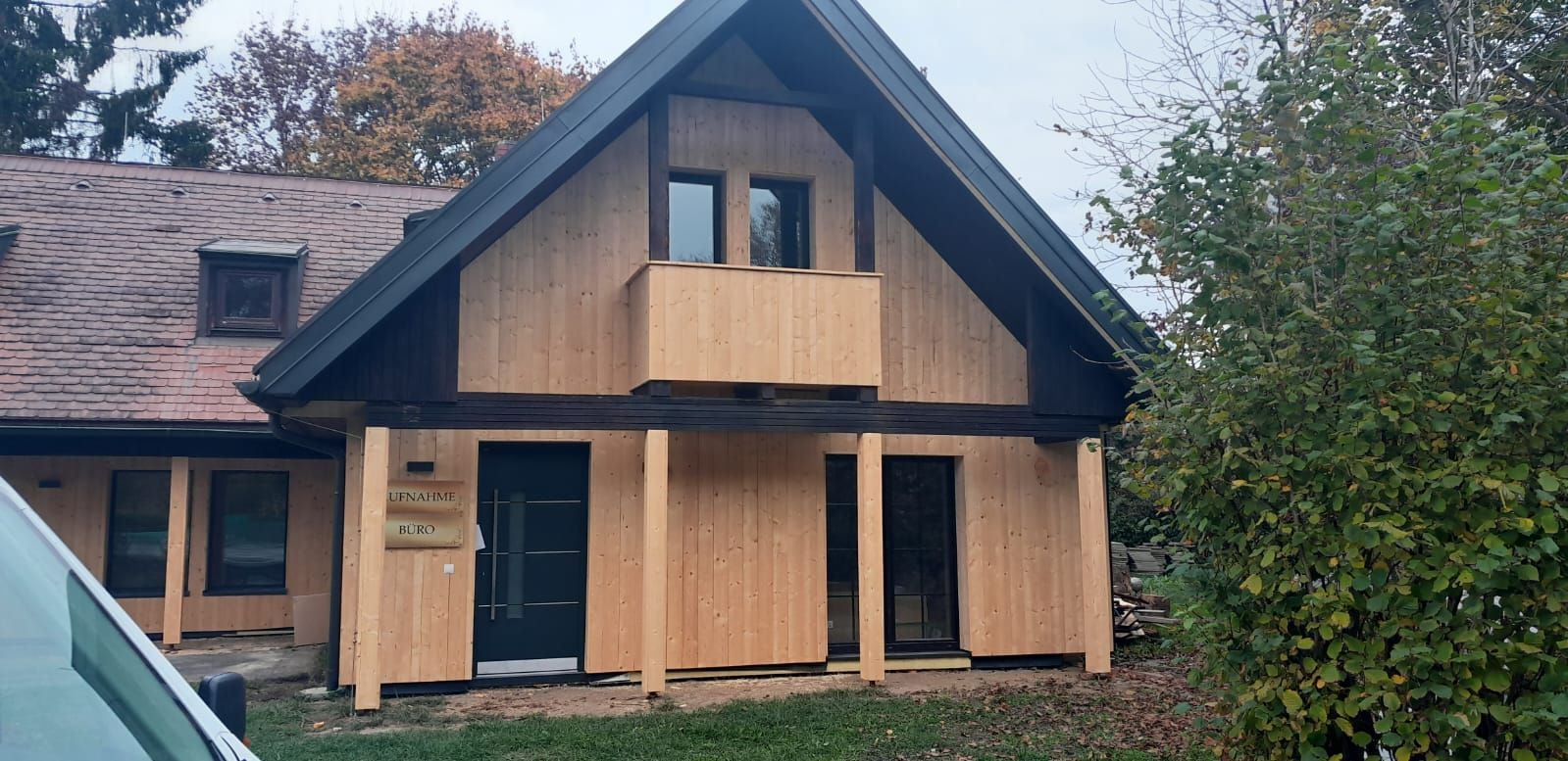 Ein Haus mit einer Holzfassade mit schwarzem Dach und einem davor geparkten Auto.