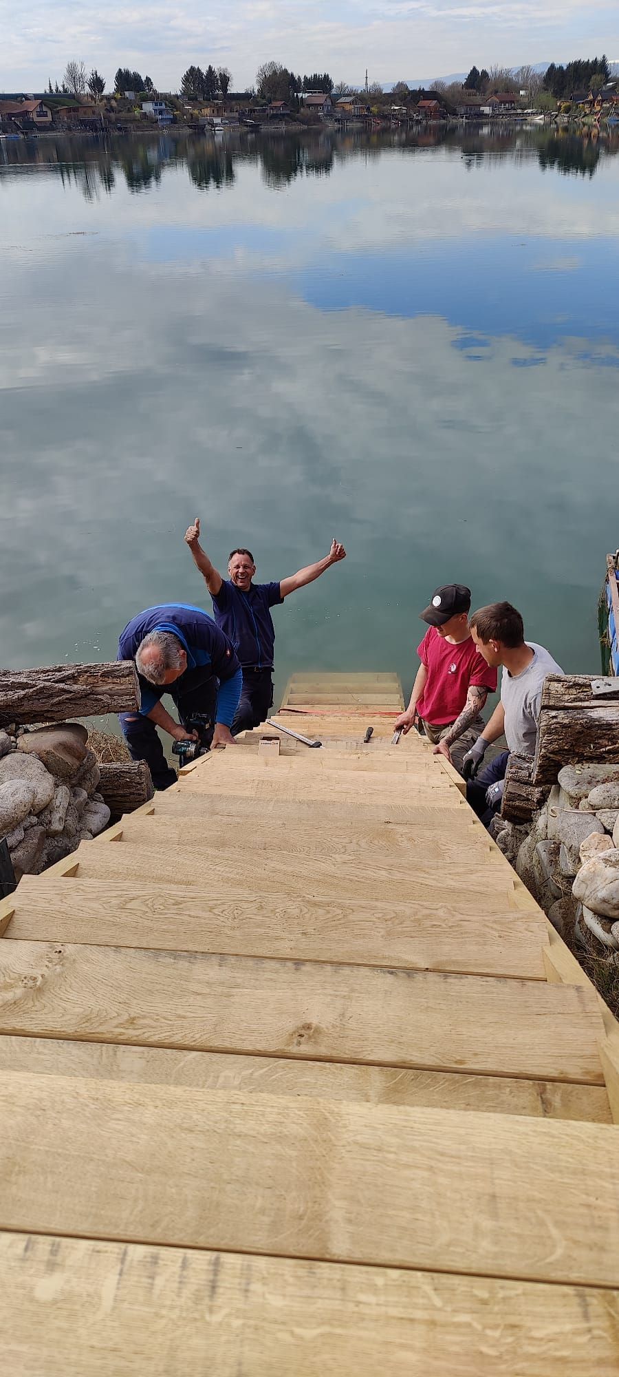 Eine Gruppe von Menschen steht auf einem Holzsteg neben einem See.