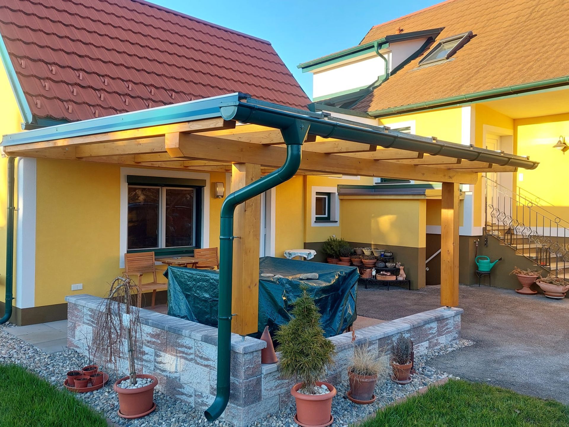 Ein gelbes Haus mit einer Pergola und einer grünen Dachrinne