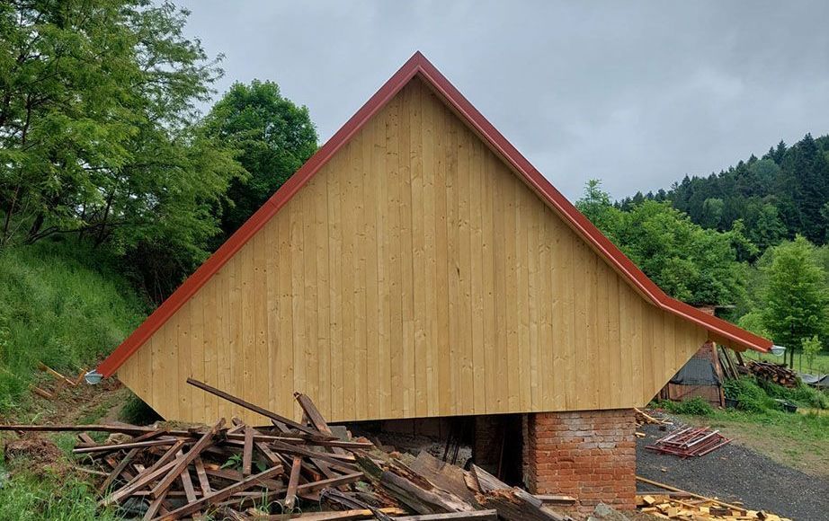 Ein Holzgebäude mit einem neuem rotem Dach und Bäumen im Hintergrund