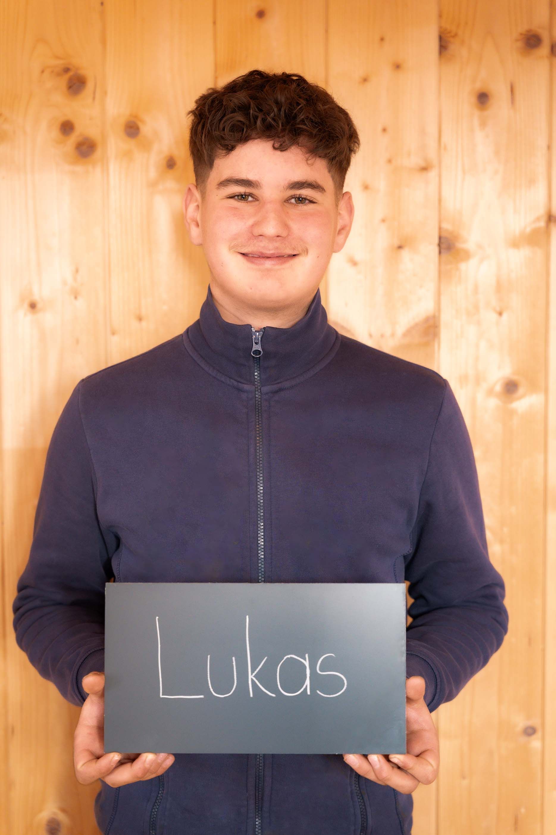 Ein junger Mann hält ein Schild mit der Aufschrift „Lukas“.