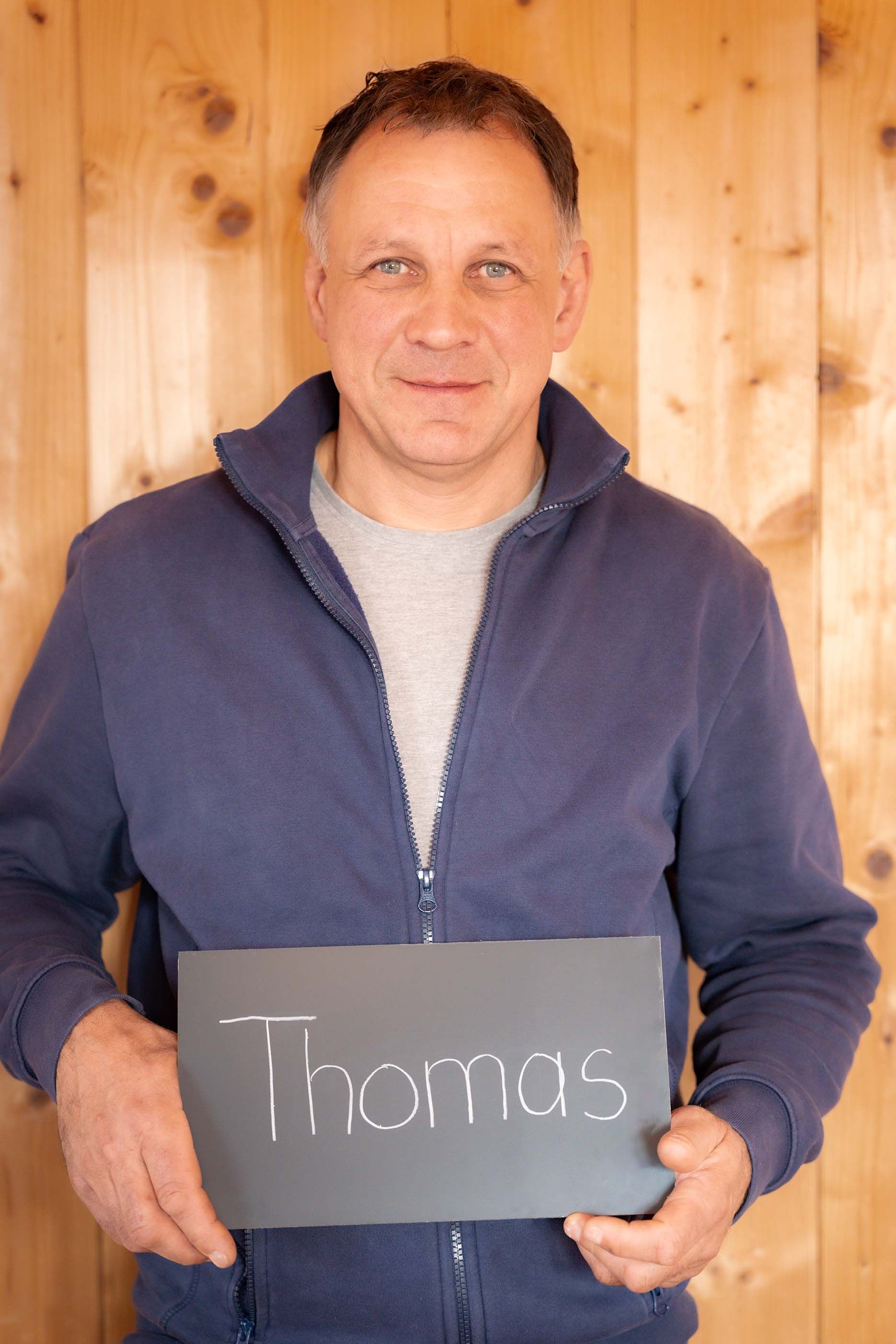 Ein Mann in einer blauen Jacke hält ein Schild mit der Aufschrift „Thomas“.
