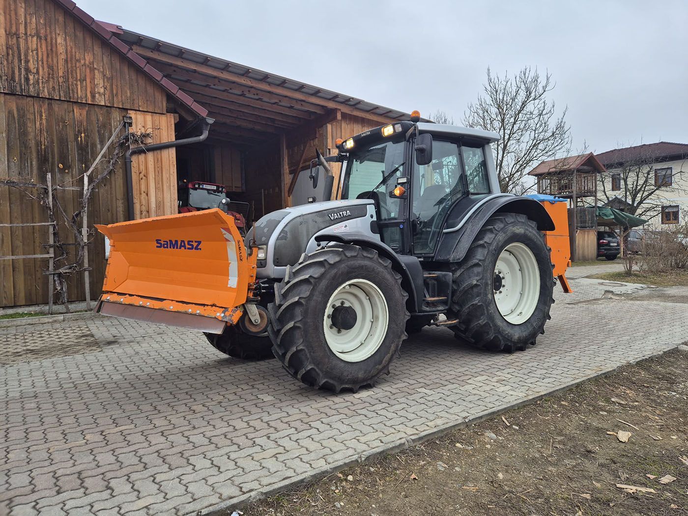 Vor einer Scheune steht ein Traktor mit angehängten Pflug.