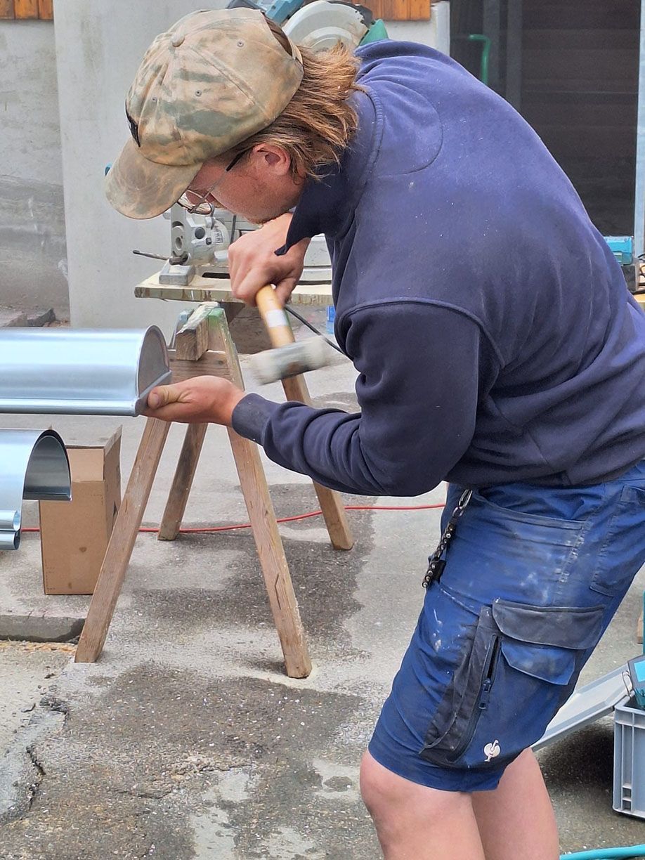 Ein Mann bearbeitet mit einem Hammer ein Metallrohr