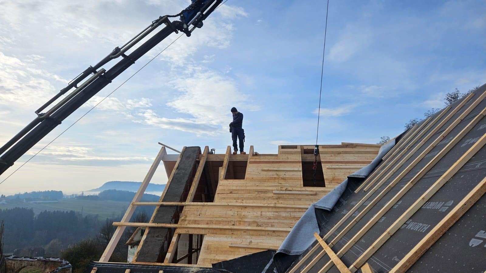 Ein Mann steht auf einem Holzdach, im Hintergrund ist ein Kran zu sehen.