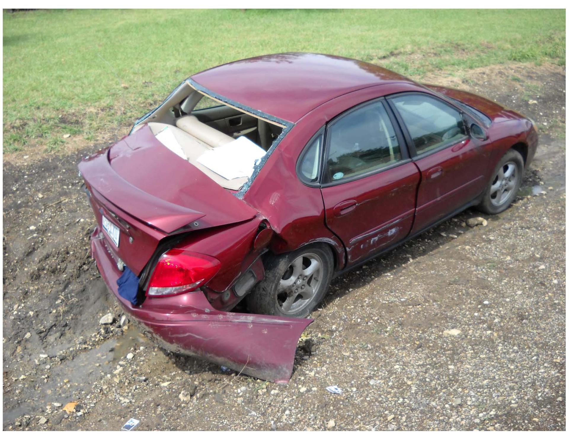 A red car with a broken windshield is sitting in the dirt