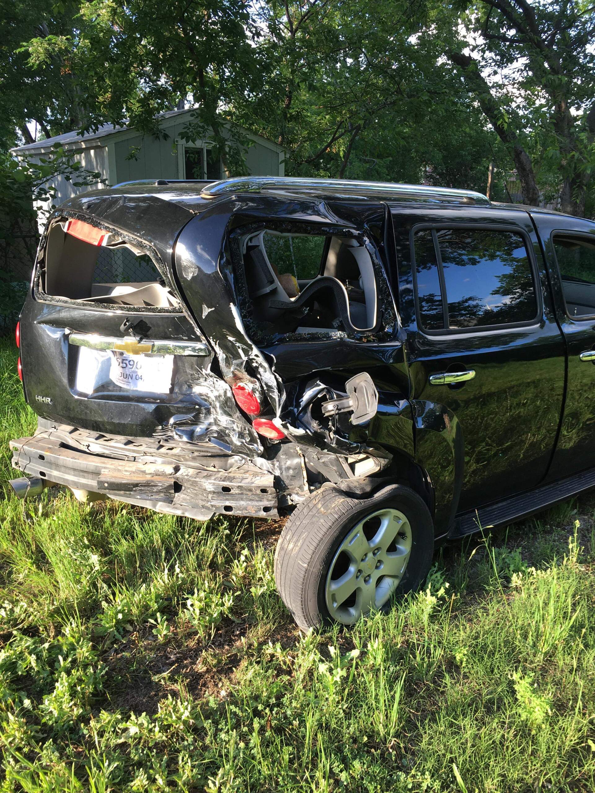 A black suv has crashed into a tree and is sitting in the grass.