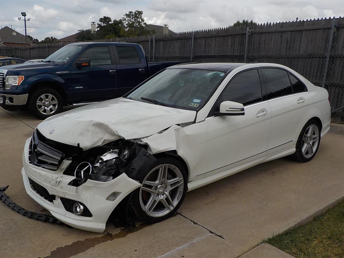 A white car with a damaged front end is parked next to a blue truck.