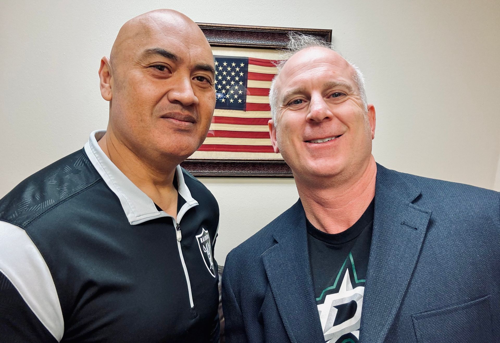 Two men are posing for a picture in front of an american flag.