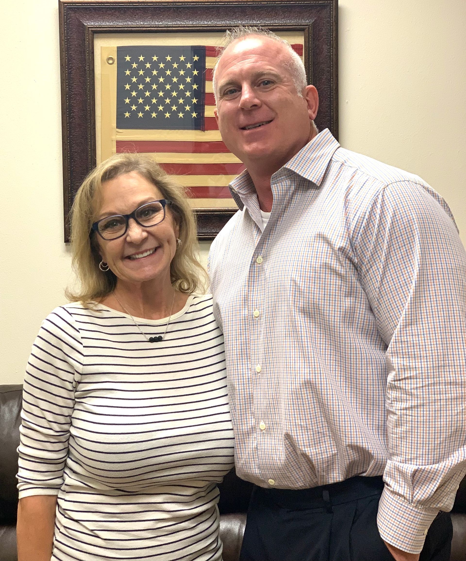 A man and a woman are posing for a picture in front of an american flag.