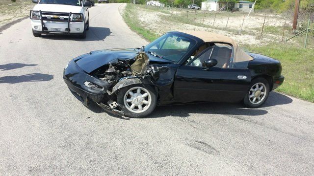 A black sports car with the top down is sitting on the side of the road.