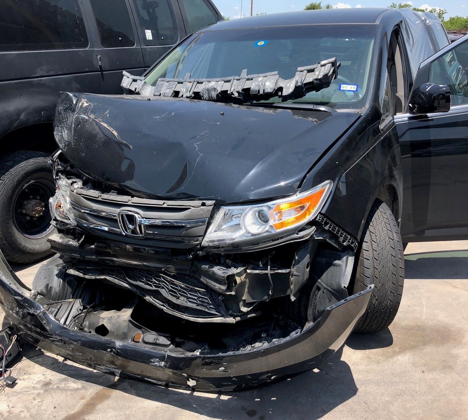 A black car with a damaged front bumper is parked in a parking lot