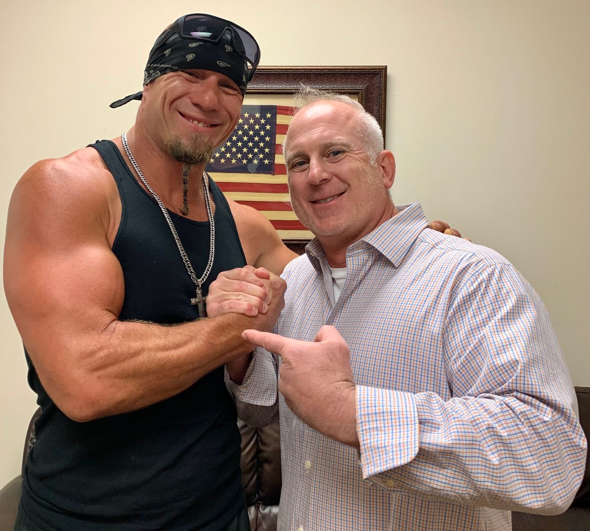 Two men are posing for a picture in front of an american flag.