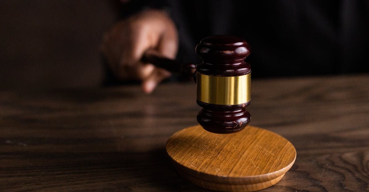 A judge is holding a wooden gavel on a wooden table.