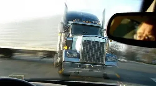 A semi truck is driving down a highway next to a car.