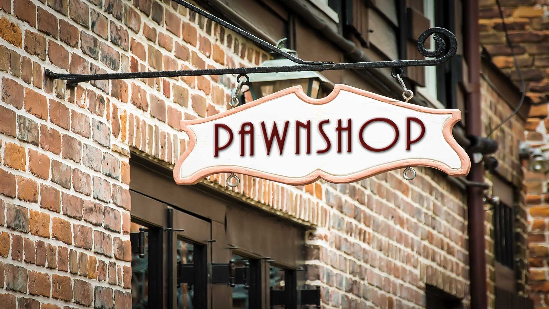 Hanging pawnshop sign on a brick building exterior.