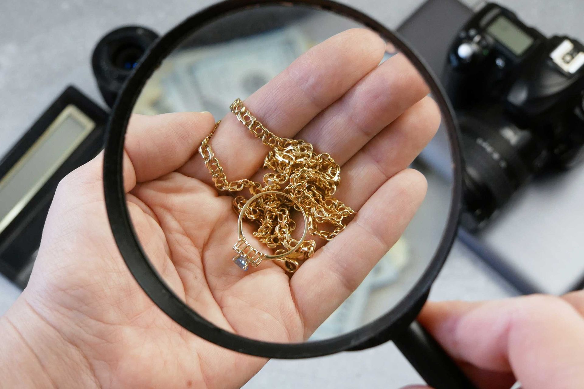 Magnifying glass inspecting gold jewelry held in an open hand. Magnifying glass inspecting gold jewelry held in an open hand.