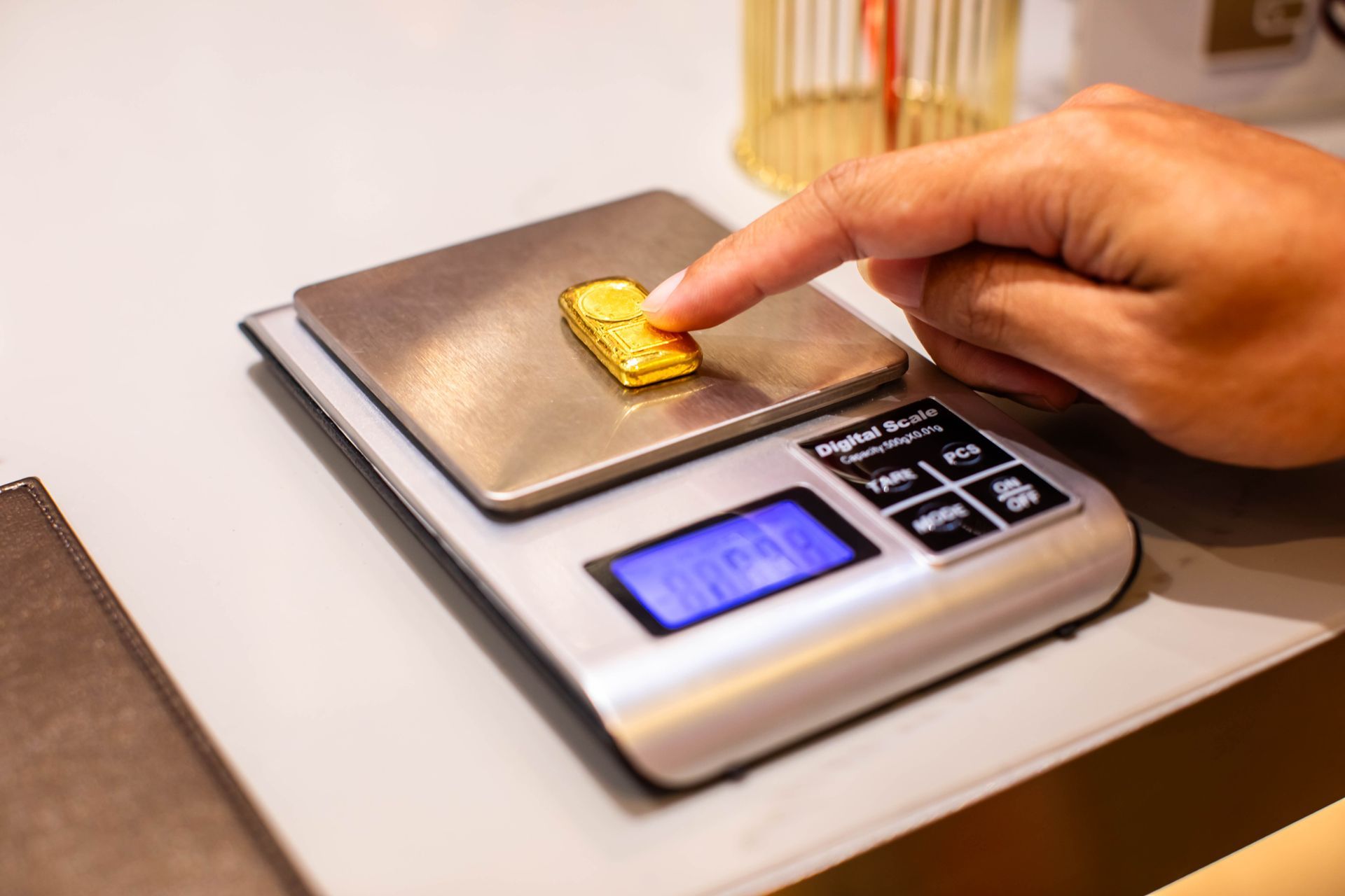 Close-up of a hand pressing a small gold bar into a small, electronic weight.